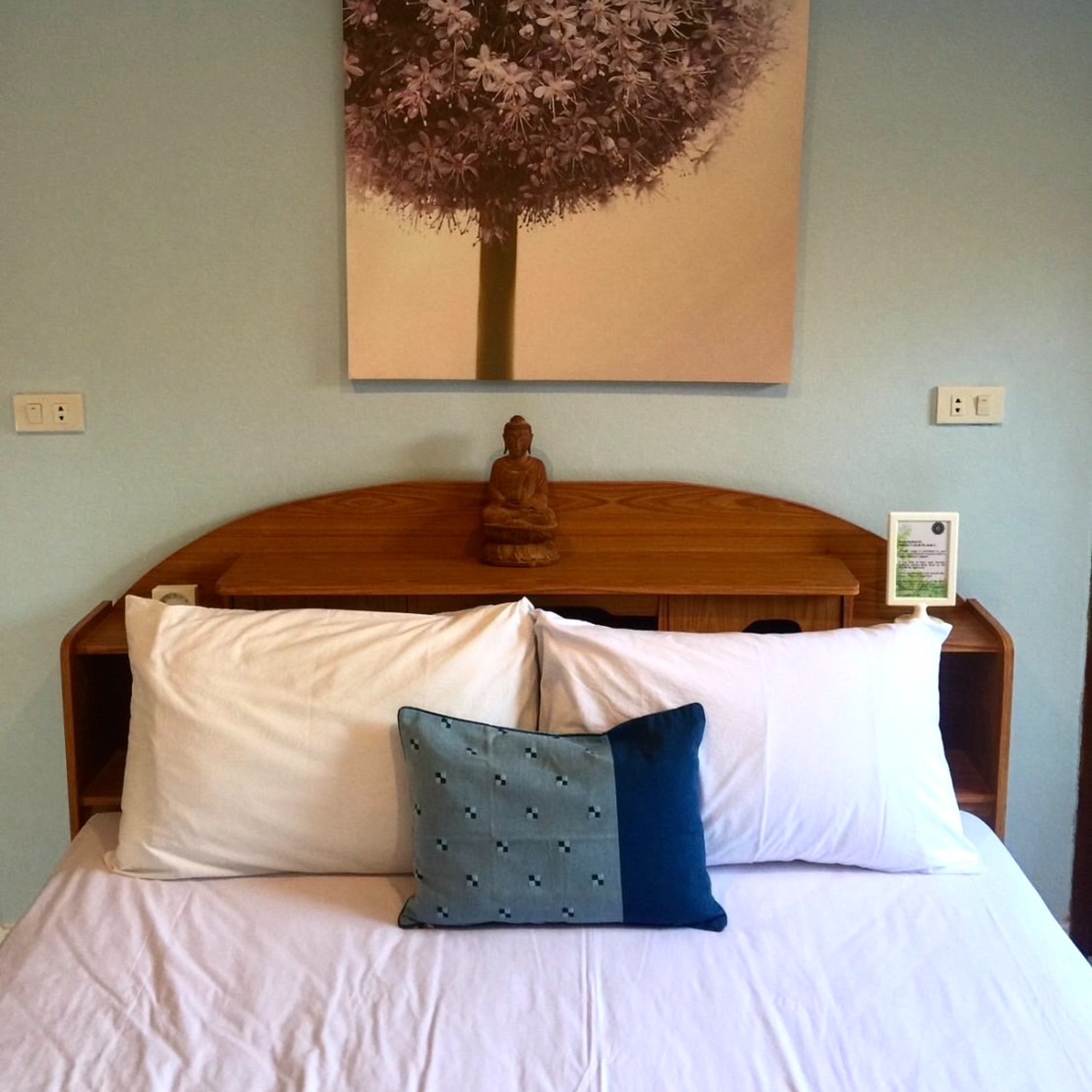A wooden headboard with a Buddha statue and a soft floral painting in the Standard Double Room at Lyndale Lodge